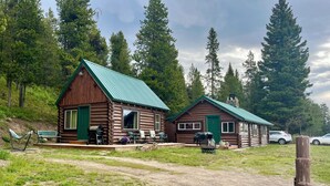 Two log cabins with green roofs, outdoor seating, and a dirt path. - Harvey’s River Retreat 30 minutes from Yellowstone (Island Park)