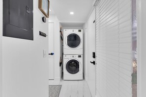A laundry room with two stacked washing machines, a door with a sign, and a window with blinds. - Stunning Designer Studio with Luxury Finishes (Deerfield Beach)