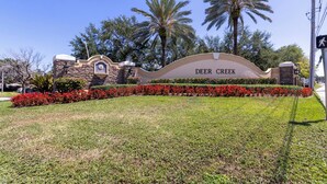 Señal de Deer Creek, con un muro de piedra, flores rojas y palmeras al fondo.