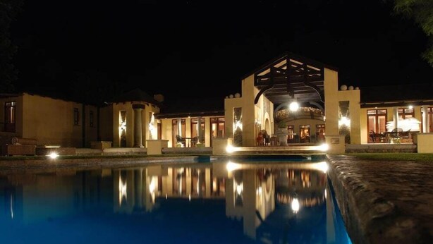 Vue nocturne d’un espace piscine avec un bâtiment doté d’un patio couvert et de sièges extérieurs.