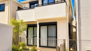 A modern two-story residential building with a balcony, large windows, and a gated entrance. - 2-Min Walk to Koya Station | Brand-New 4BR Private House | Free Parking & Wi-Fi (足立区)
