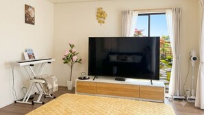 A bedroom with a bed, a TV, a desk with a chair, a potted plant, and a window with curtains. - 2-Min Walk to Koya Station | Brand-New 4BR Private House | Free Parking & Wi-Fi (足立区)