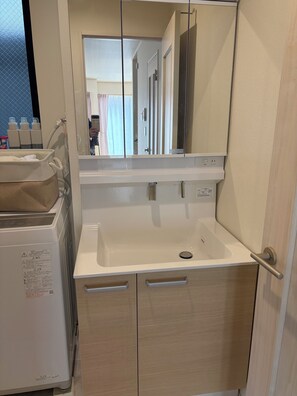 A bathroom with a white sink, a mirror, a towel rack, and a small cabinet. - 2-Min Walk to Koya Station | Brand-New 4BR Private House | Free Parking & Wi-Fi (足立区)