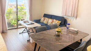 A room with a sofa, a dining table, a small plant, and a view through a sliding door. - 2-Min Walk to Koya Station | Brand-New 4BR Private House | Free Parking & Wi-Fi (足立区)
