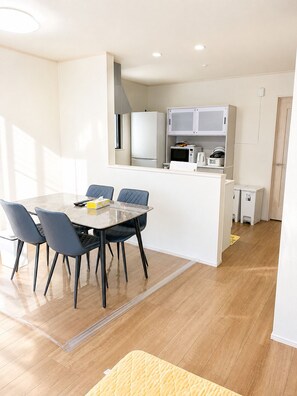 A compact kitchen with a dining area, including a table with chairs, a microwave, and a refrigerator. - 2-Min Walk to Koya Station | Brand-New 4BR Private House | Free Parking & Wi-Fi (足立区)