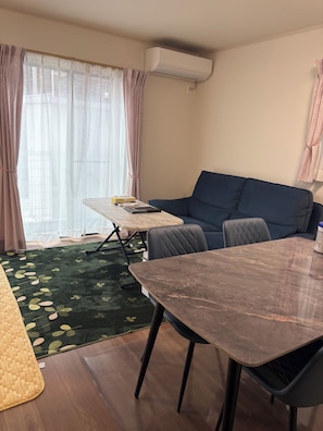 Een kamer met een eettafel, een bank, een klein tafeltje met boeken en een airconditioner.