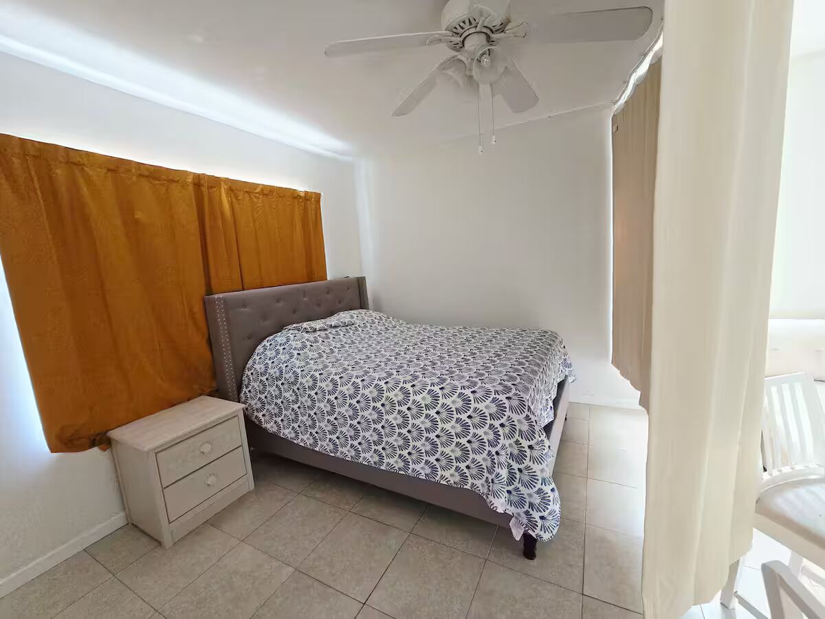 Un dormitorio con cama, mesita de noche y ventilador de techo.