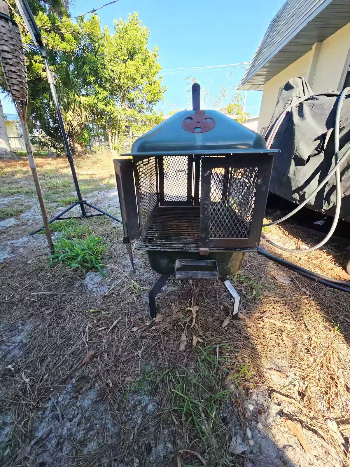 A barbecue grill outdoors with a metal grate, a chimney, and a protective mesh cover.