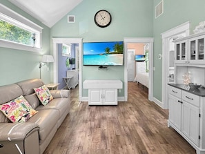 A living room with a sofa, TV, and kitchen area. - Seaglass Village 224 - Windswept (Wells)
