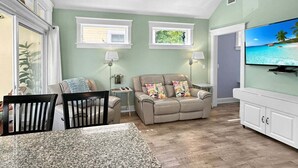 A living room with a sofa, TV, and dining area. - Seaglass Village 224 - Windswept (Wells)