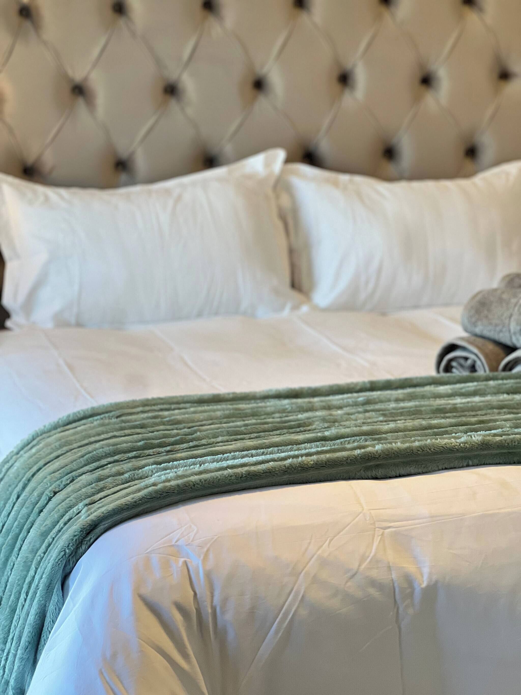 A neatly made bed with white bedding and a green throw blanket.