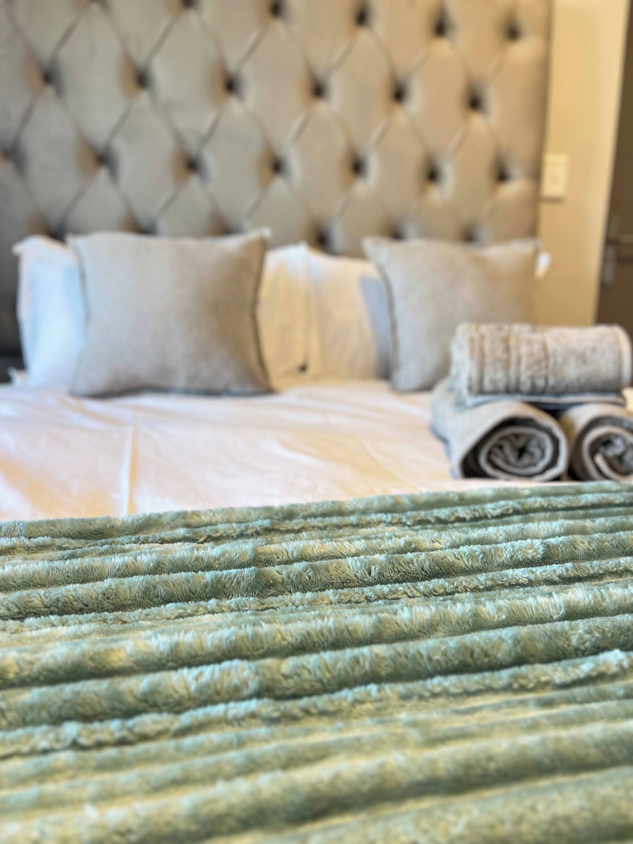 A bed with a tufted headboard, pillows, and rolled towels.
