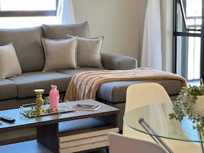 A modern living room with a sofa, a glass coffee table, and a side table. - Luxury Apartment Overlooking the River (Johannesburg)