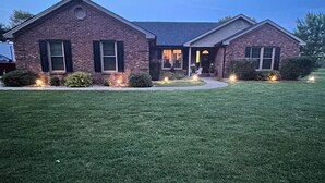 A two-story brick house with a front porch, a well-maintained lawn, and outdoor lighting.