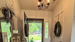 A hallway with a wooden bench, a chandelier, a patterned rug, and a door with a wreath.
