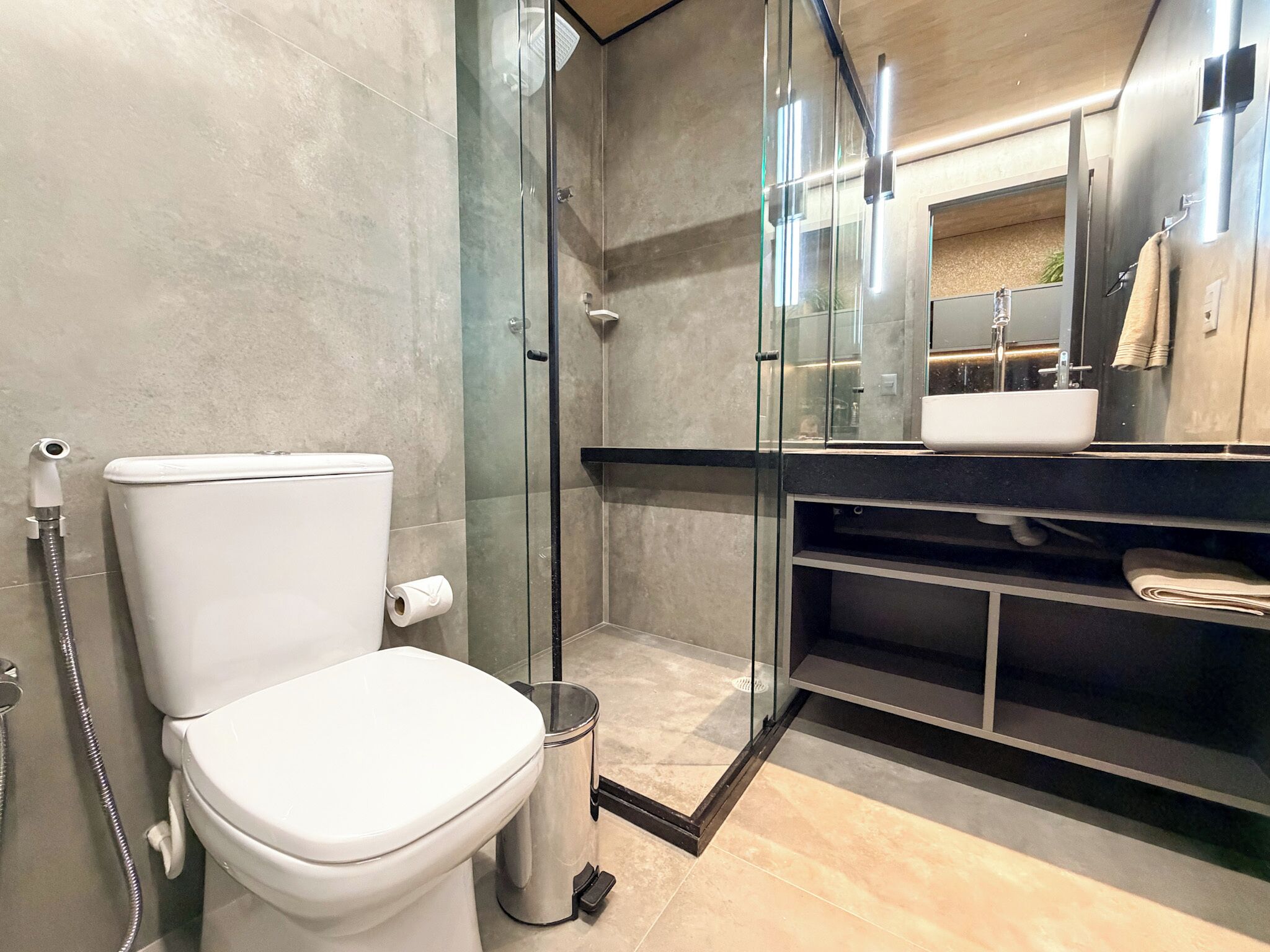 A modern bathroom with a toilet, glass shower enclosure, and a sink with a mirror above it.