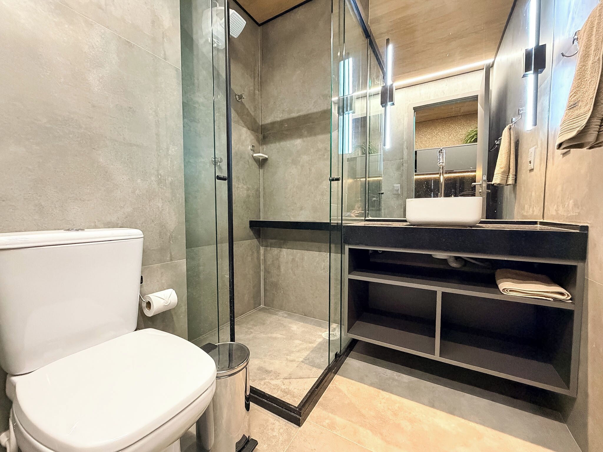 Un baño moderno con cabina de ducha de vidrio, un inodoro blanco, un lavabo con espejo y un perchero para toallas.