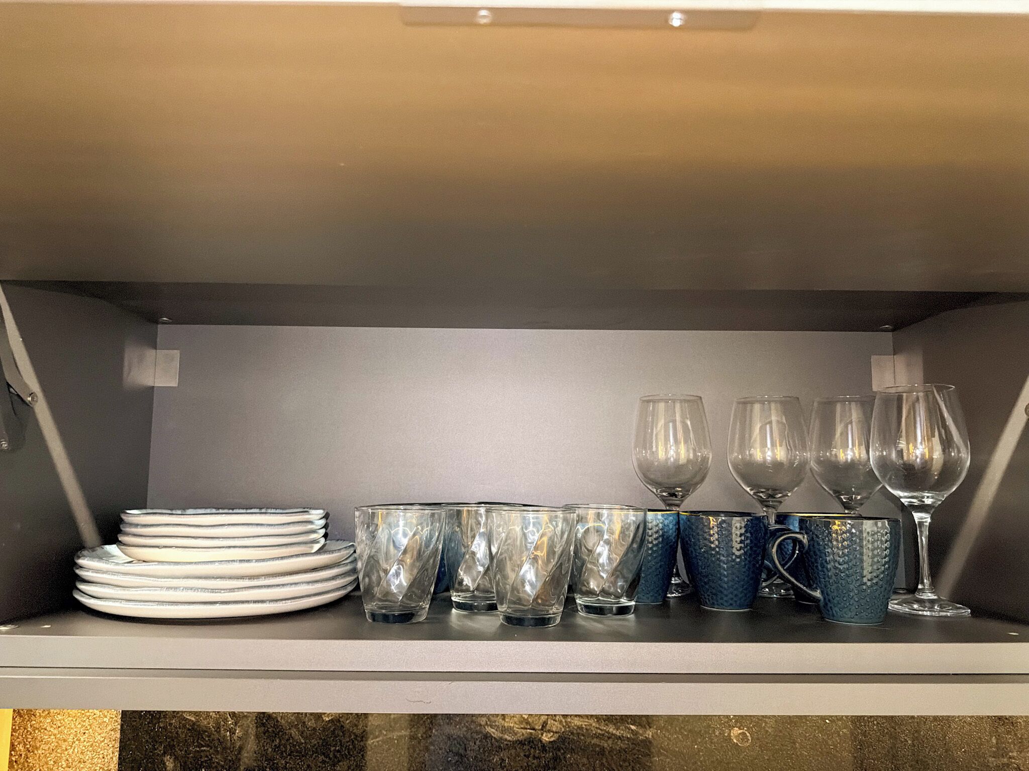 A shelf with stacked plates, clear glasses, and blue textured mugs.