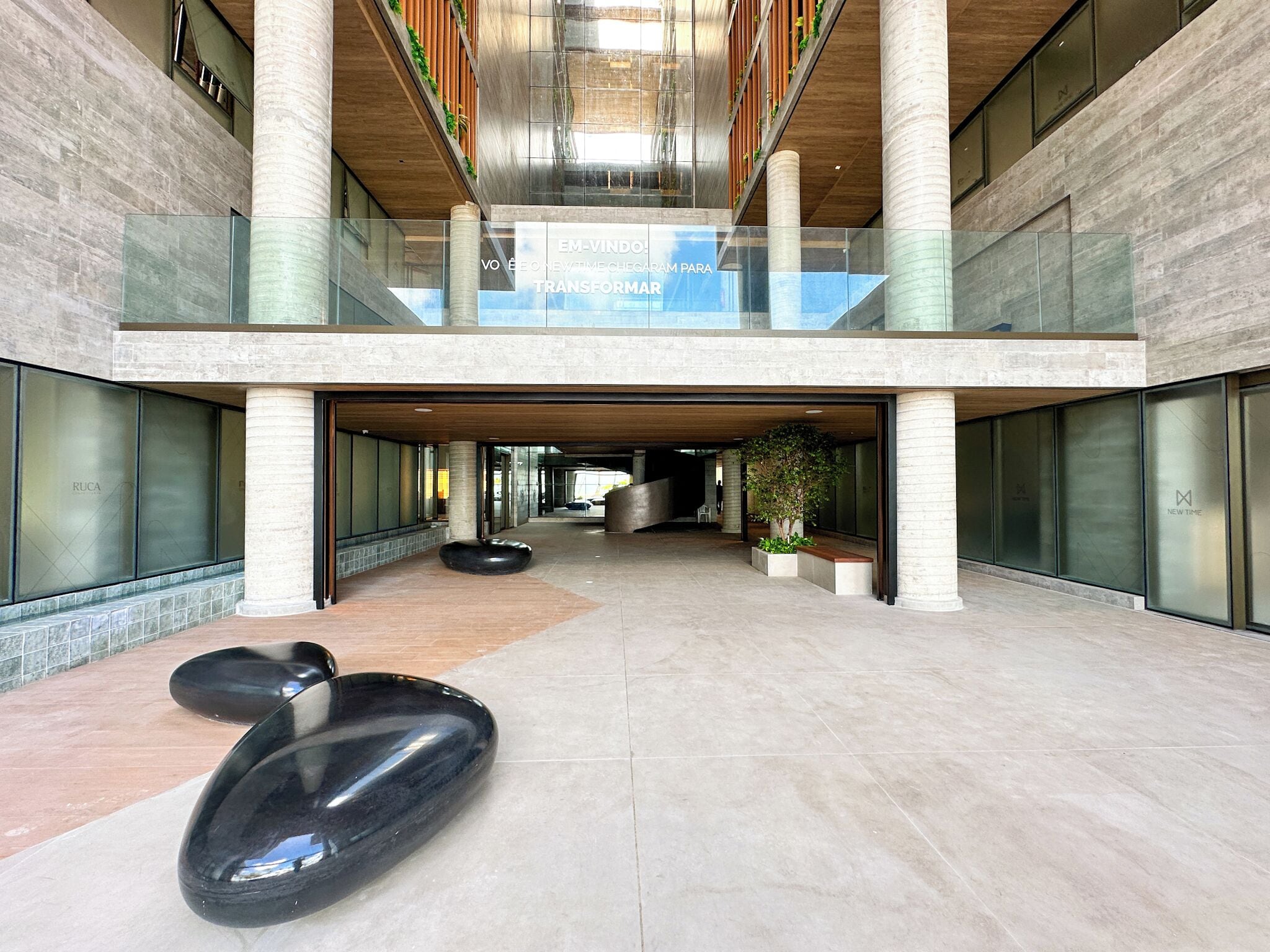 Un bâtiment moderne doté d’un atrium en verre, d’une colonne centrale et d’une enseigne sur laquelle on peut lire : « EM-VINDO VO É CONEXÃO PARA TRANSFORMAR. »