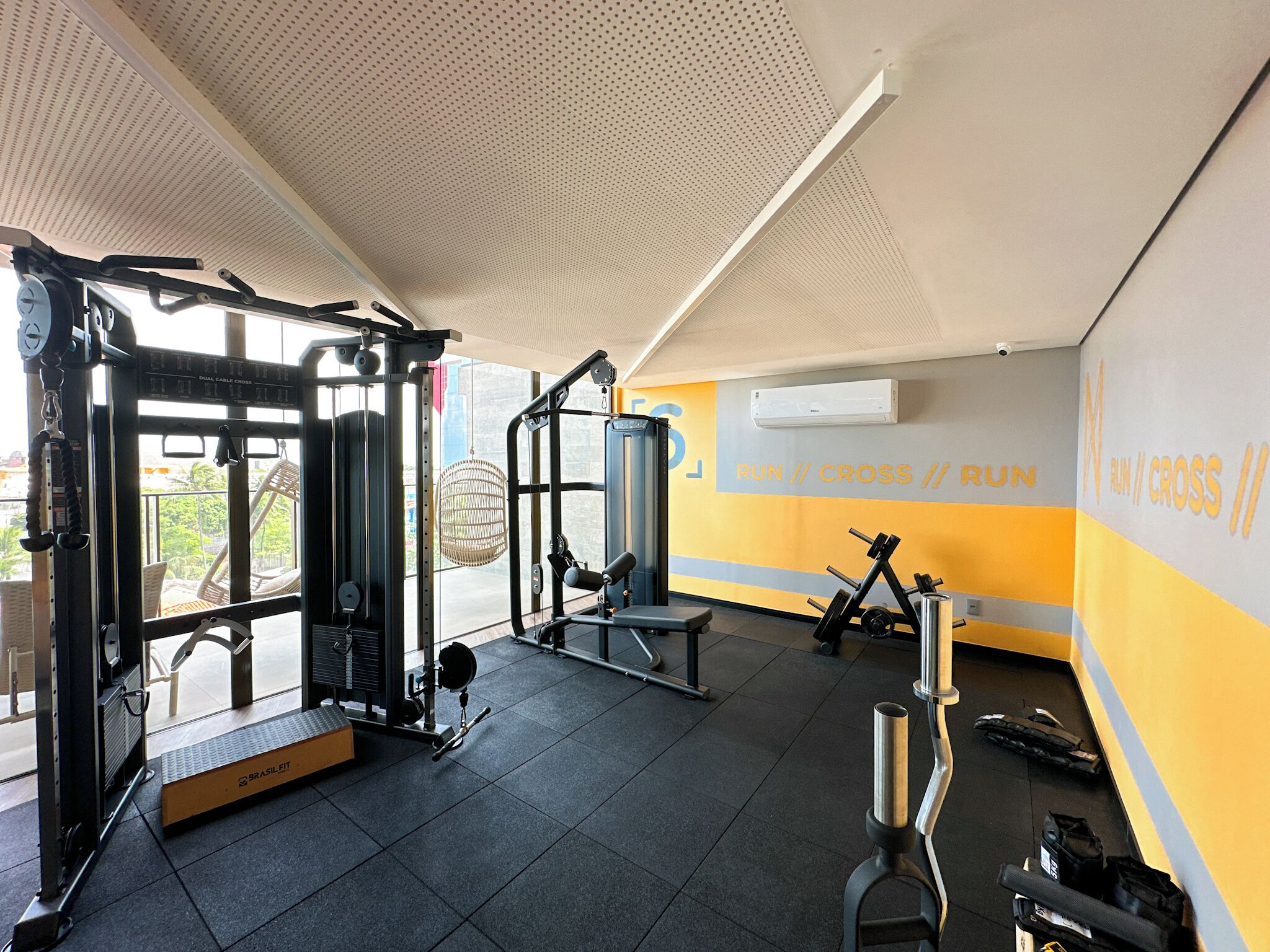 A gym with various exercise equipment, a wall with motivational text, and a view of the outdoors.