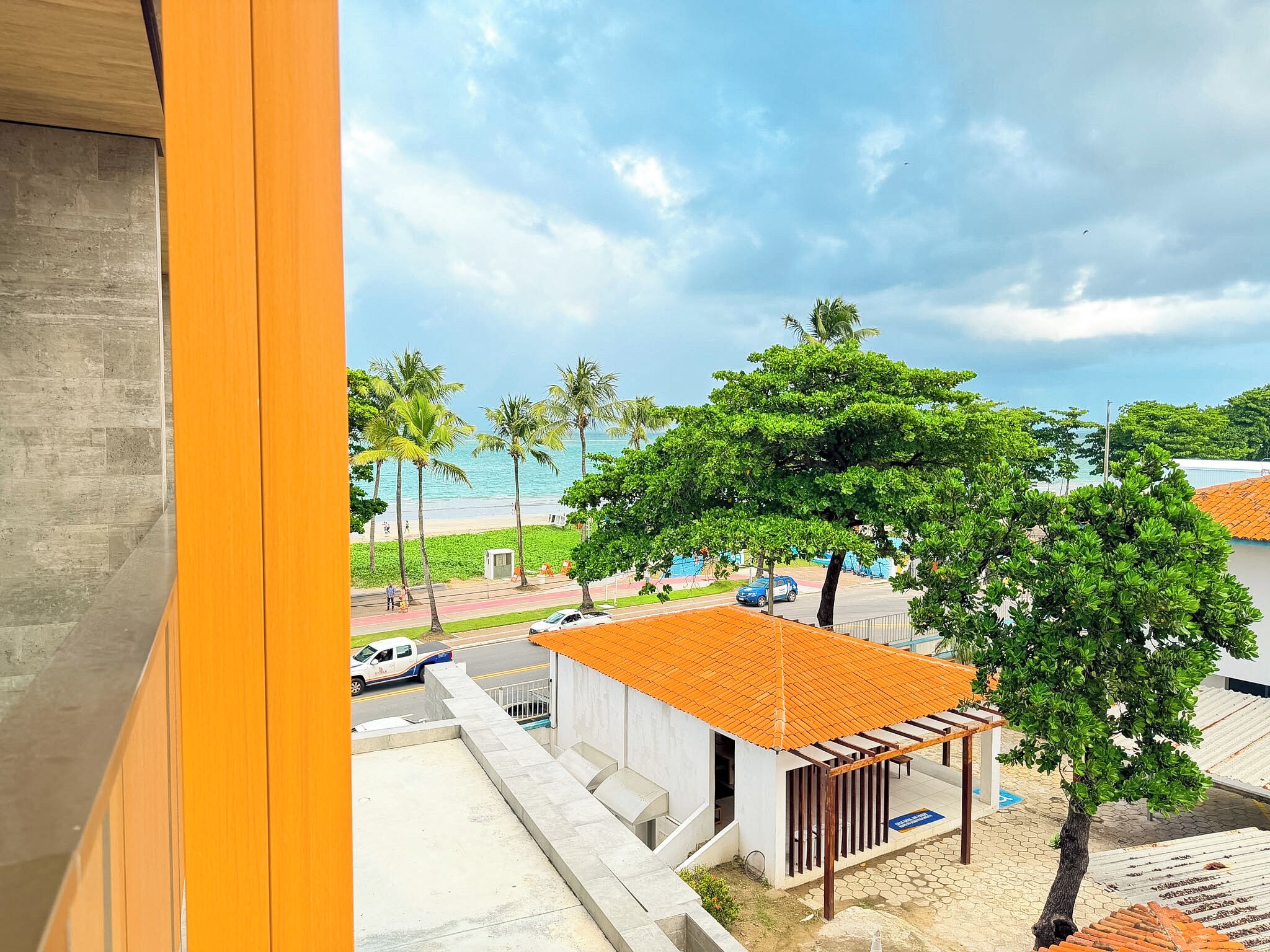 A coastal view with a beach, palm trees, and a small building with a tiled roof.