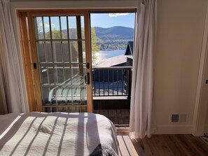 Un dormitorio con una cama grande, una puerta corrediza de vidrio que da a un balcón con vistas a un lago y montañas.