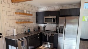 Een moderne keuken met een roestvrijstalen koelkast, magnetron en vaatwasser, houten kastjes en een betegelde spatwand.