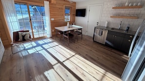 Een houten interieur met een eethoek, keuken en grote ramen.