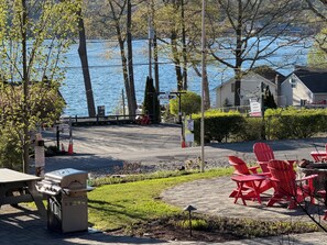 Un patio junto al lago con sillas Adirondack rojas, una parrilla y vista al agua.