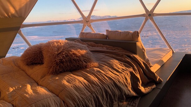 A cozy, insulated sleeping area with a view of a snowy landscape through a geometric window structure.