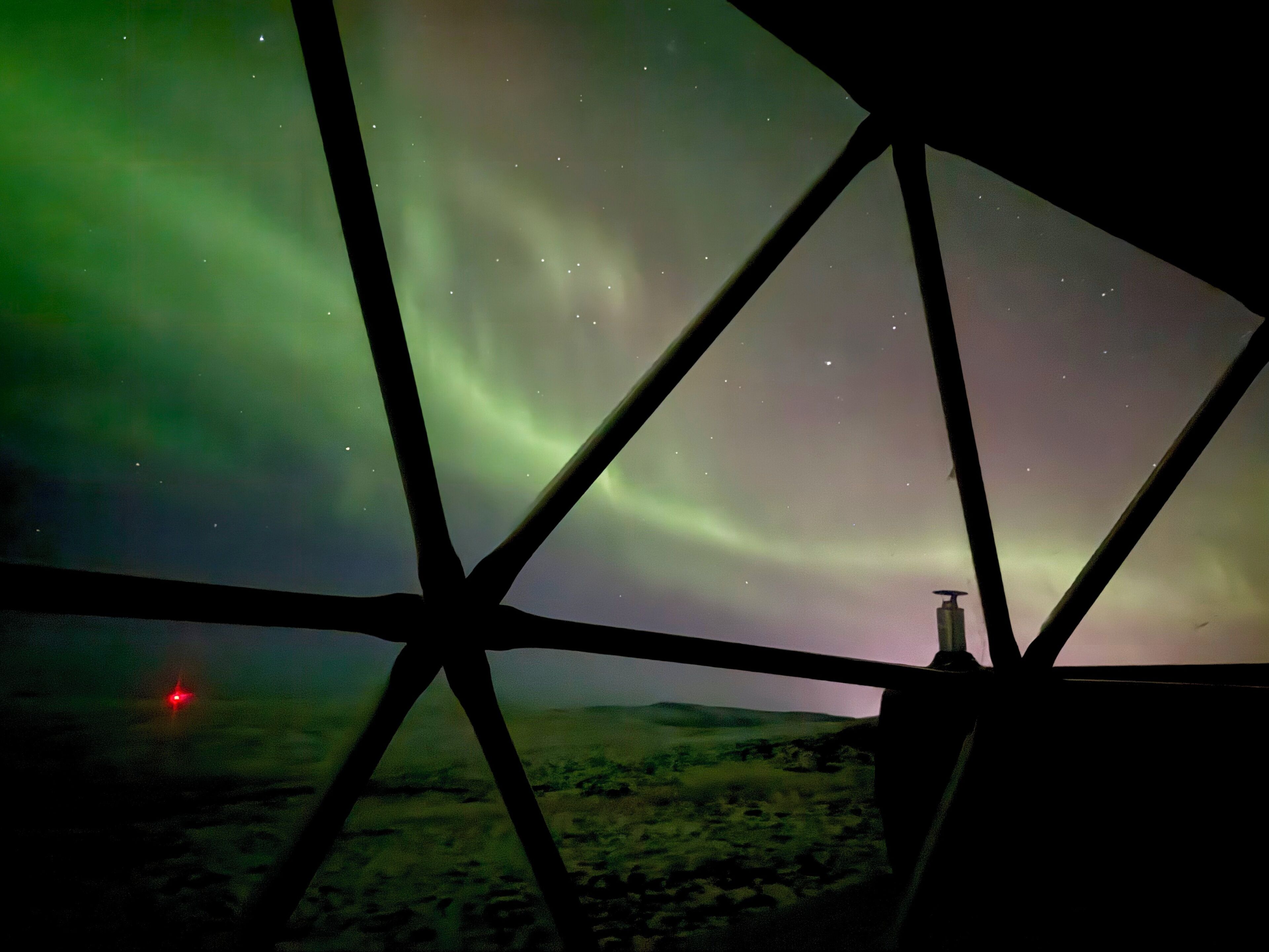 Una vista attraverso una finestra con cornice geometrica, un paesaggio con una piccola costruzione, e l'aurora boreale.