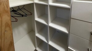 A white closet with multiple shelves and drawers, a wooden door, and a coat rack with hangers.