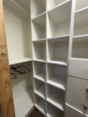 A white closet with multiple shelves and drawers, a wooden door, and a coat rack with hangers. - El Rincon de Paz, House equipped at 11 km airport (Puerto Montt)