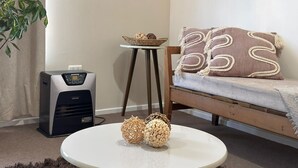 A living room with a round table, a sofa, a standing heater, and a plant.