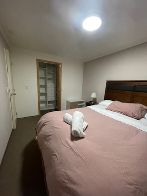 Une chambre à coucher comprenant un lit, une table de chevet, une lampe, une tête de lit en bois et une armoire avec une porte coulissante.