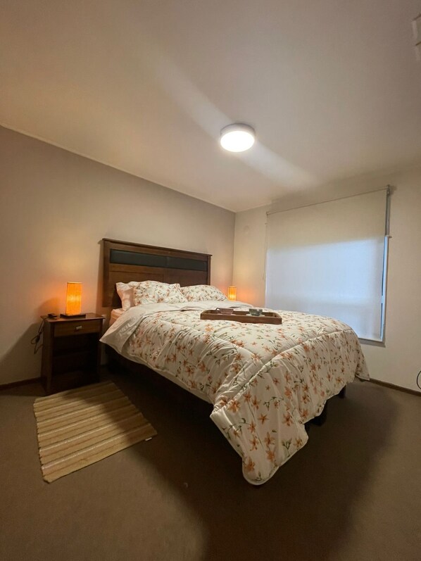 A bedroom with a bed, bedside lamps, a nightstand, a window, and a ceiling light. - El Rincon de Paz, House equipped at 11 km airport (Puerto Montt)