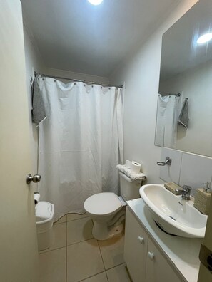 Une petite salle de bain propre, équipée de toilettes, d’un lavabo et d’un rideau de douche.