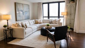 A living room with a sectional sofa, a round coffee table, a black armchair, a white rug, and a large abstract painting on the wall. - Stunning 3-bedroom condo 
Labor Day Special, book now! (Destin)