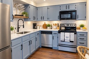 A kitchen with light blue cabinets, a stainless steel refrigerator, a black microwave, a stove, and a dishwasher. - Newly Renovated 3BR Destin Condo across from Beach — Ask About Winter Rates (Destin)