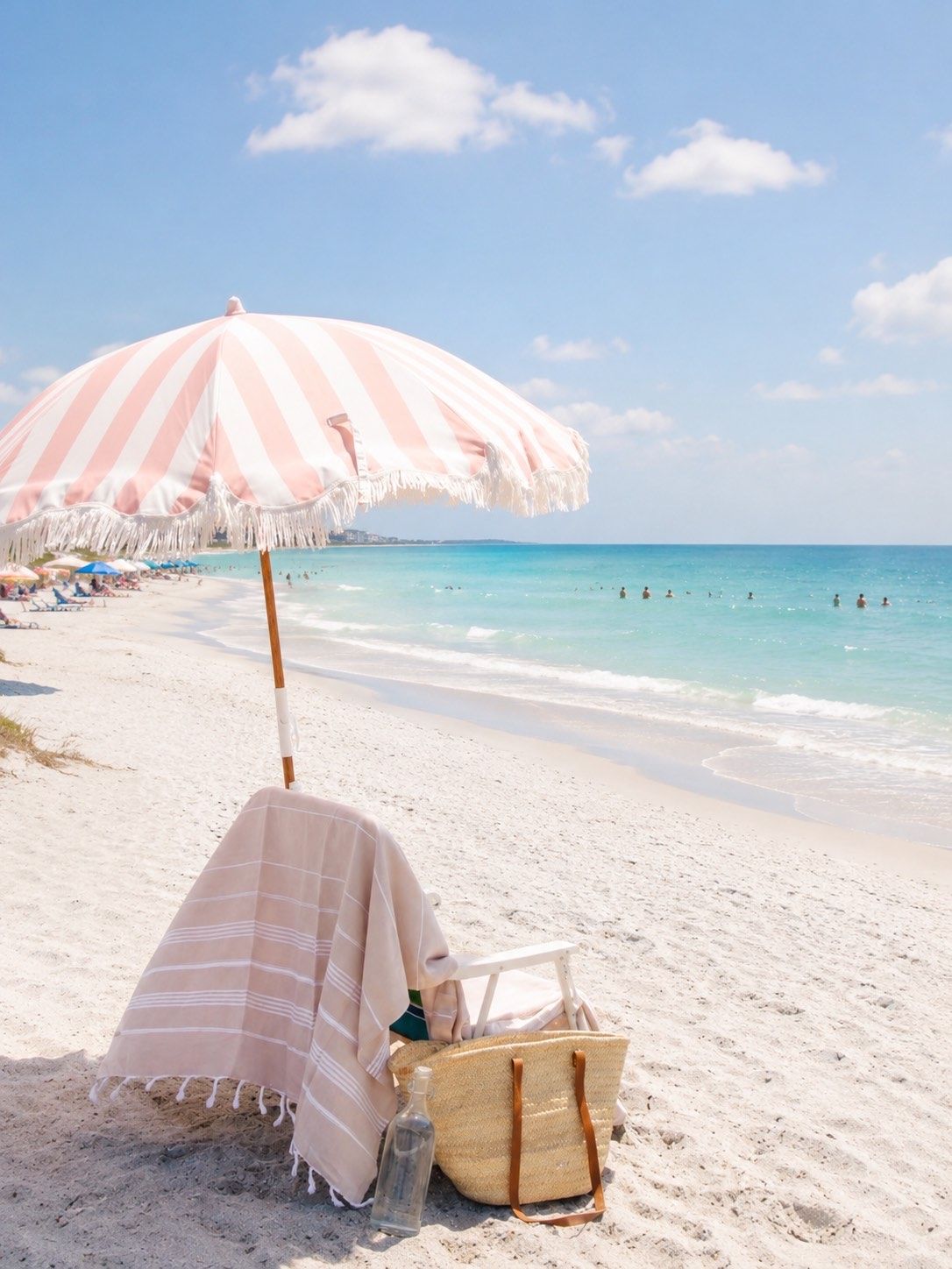 Une scène de plage avec un parasol rayé, une chaise de plage et un sac en paille posés sur le sable.