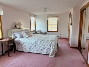 Ein Schlafzimmer mit Bett, Nachttisch, Lampe und zwei Fenstern mit Jalousien.