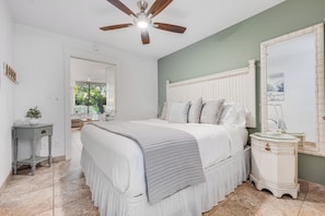 A bedroom with a bed, a nightstand, a mirror, a ceiling fan, and a view of the outdoors. - Steps to Sugar Beach | 2 King Beds, Pool, Hot Tub & AC in North Kihei (Kihei)