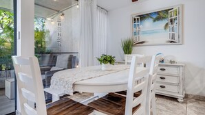 A dining area with a white table, wooden chairs, a white cabinet, and a painting of a beach scene. - 2BR Kihei Condo | Walk to Sugar Beach, Pool, Hot Tub & 2 King Beds (Kihei)