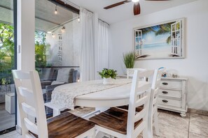 A dining area with a white table, wooden chairs, a white cabinet, and a painting of a beach scene. - Steps to Sugar Beach | 2 King Beds, Pool, Hot Tub & AC in North Kihei (Kihei)
