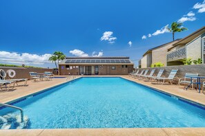 Une piscine avec des chaises longues, un bâtiment doté d’un toit plat et des palmiers.