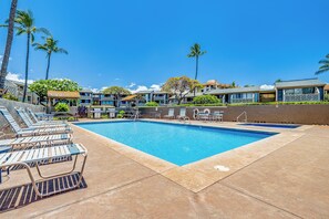 A swimming pool with lounge chairs, palm trees, and hotel buildings. - Steps to Sugar Beach | 2 King Beds, Pool, Hot Tub & AC in North Kihei (Kihei)
