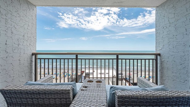 Ein Balkon mit Korbmöbeln, Blick auf den Strand und einem klaren Himmel.