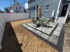 Eine Terrasse mit Tisch und Stühlen, umgeben von Kies und einer Fliesenbordur.
