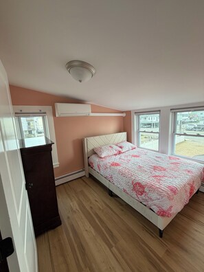 A bedroom with a bed, an air conditioning unit, a window, and a door.