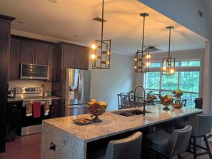 Una cocina moderna con encimeras de granito, electrodomésticos de acero inoxidable e iluminación colgante.